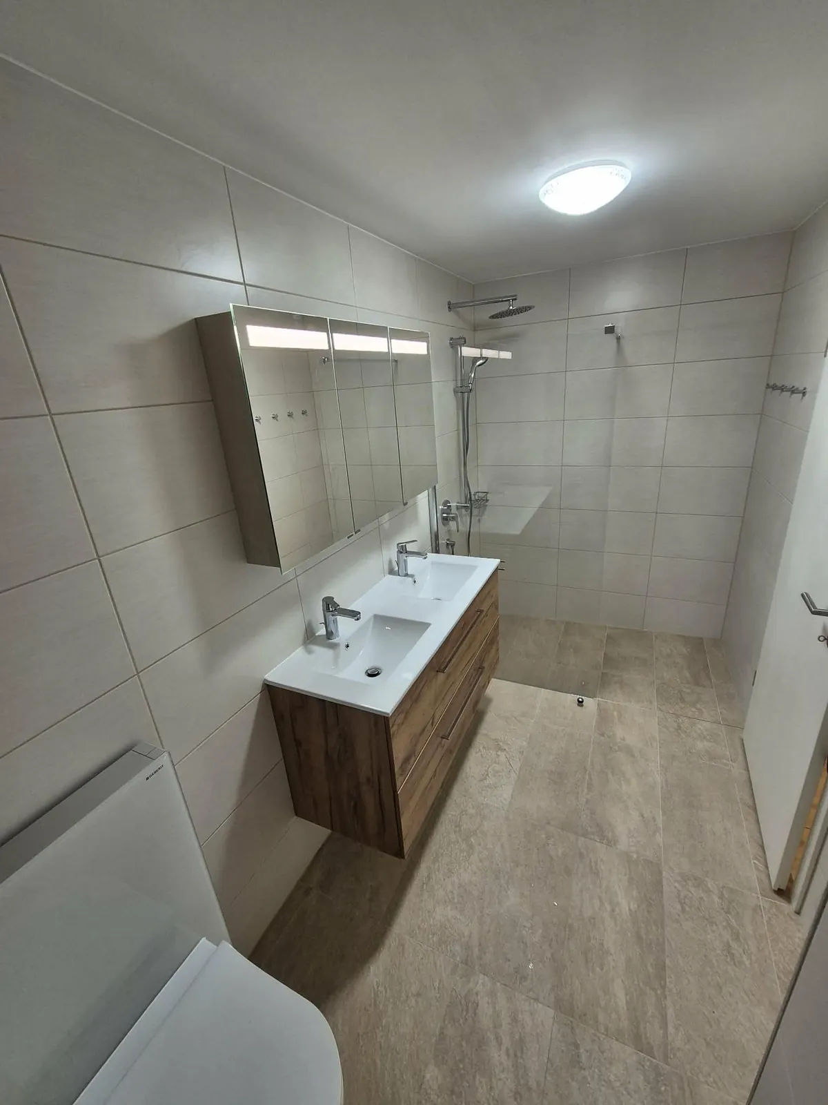 Saniertes Bad mit grossformatigen Fliesen, Doppelwaschtisch, Spiegelschrank und bodenebener Dusche